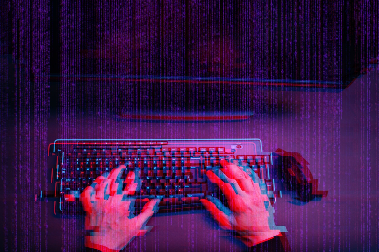 Hacker working with computer in dark room with digital interface around. Image with glitch effect.
